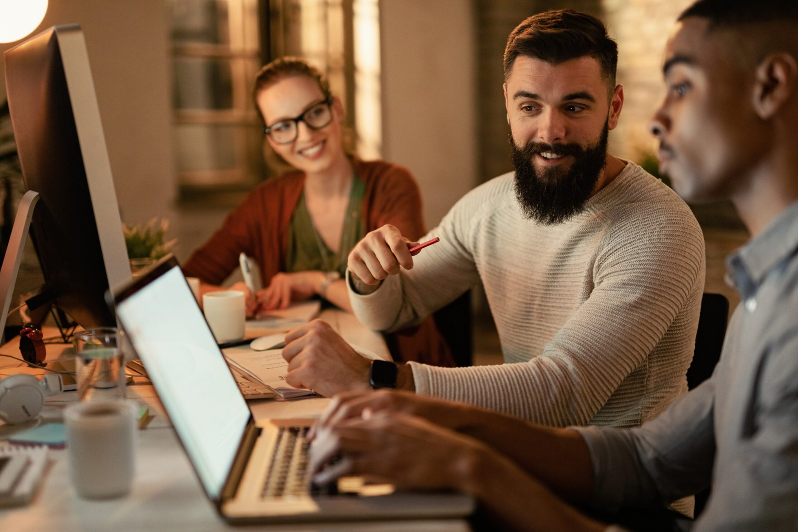 Young freelance workers using laptop while working late in the office. Focus is on man with beard.