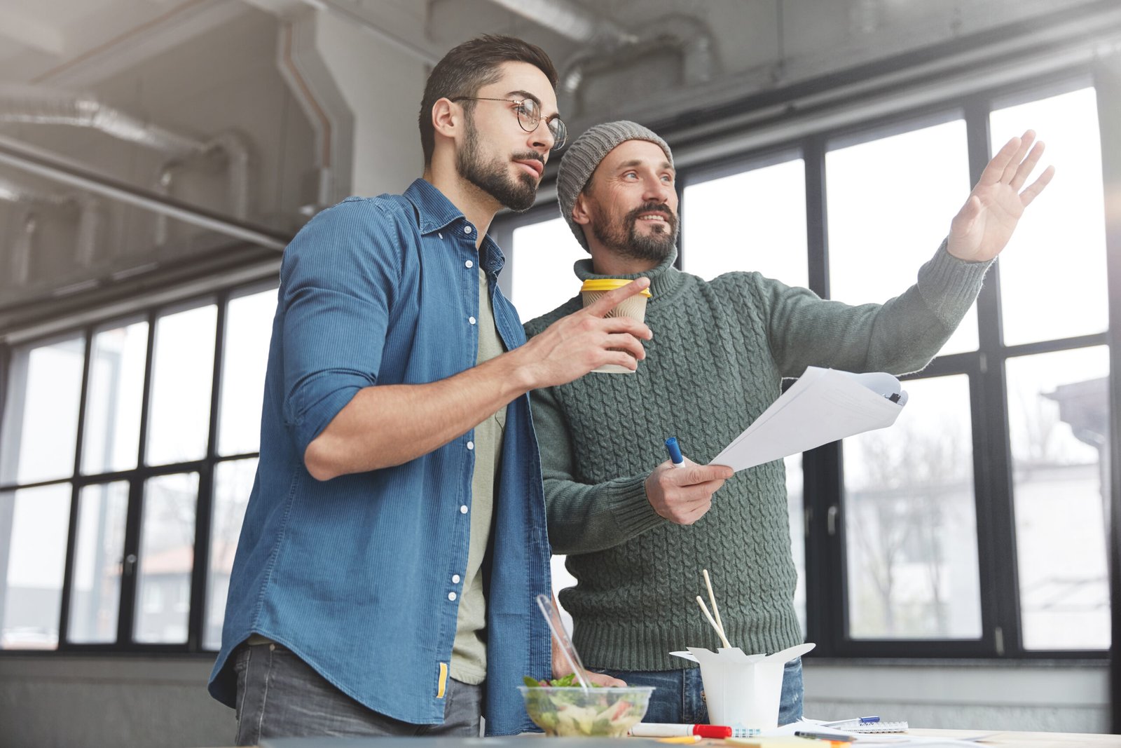 Mature bearded marketing director and his assistant choose place where conduct meeting with business patrners, points at spacious cabinet, have coffee break or lunch, prepare financial report